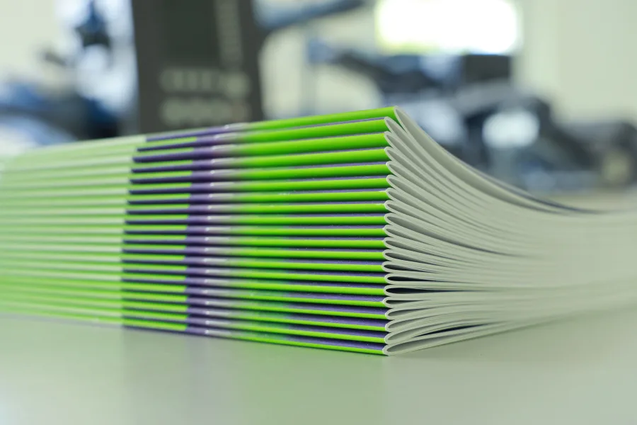 Stack of freshly printed saddle-stitched brochures with green covers in a print workshop
